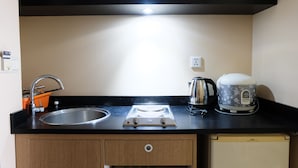 A kitchen with a sink, stove, kettle, and a small refrigerator. - Strategic And Comfy 1Br At Braga City Walk Apartment (Bandung)