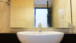 A white sink with a modern faucet, a mirror above it, and a black countertop. - Strategic And Comfy 1Br At Braga City Walk Apartment (Bandung)