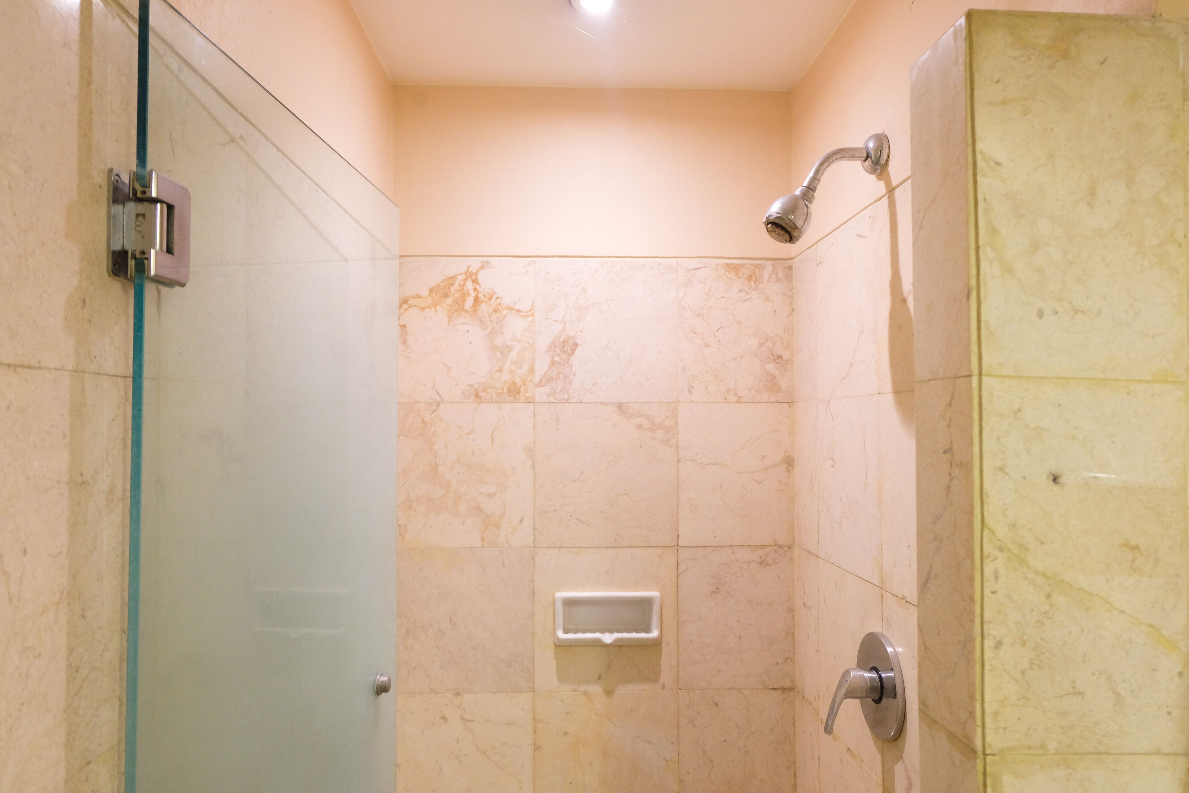 A bathroom with a glass door, a shower with a handheld showerhead, and a soap dispenser on the wall.