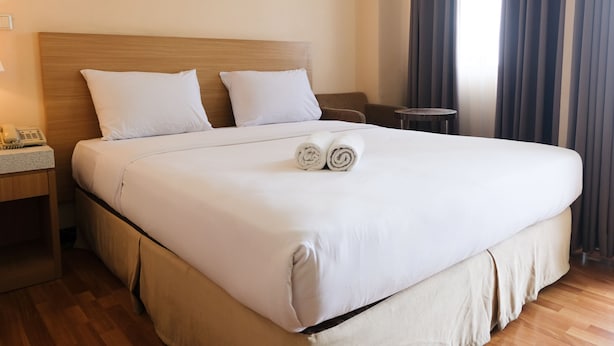 A neatly made bed with white linens, two rolled towels, a wooden headboard, a bedside table with a phone, and a small round table. - Strategic And Comfy 1Br At Braga City Walk Apartment (Bandung)