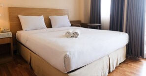 A neatly made bed with white linens, two rolled towels, a wooden headboard, a bedside table with a phone, and a small round table. - Strategic And Comfy 1Br At Braga City Walk Apartment (Bandung)