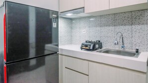 A kitchen with a black refrigerator, a sink, and a tiled backsplash. - Well Furnished And Comfy 2Br At Royal Heights Apartment (Bogor)