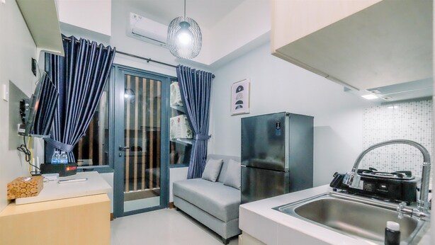 A compact kitchen with a refrigerator, sink, and a small seating area with a sofa. - Well Furnished And Comfy 2Br At Royal Heights Apartment (Bogor)