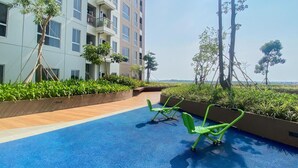 A rooftop terrace with a blue floor, green chairs, and a building with multiple balconies. - Chic And Cozy Studio At Tokyo Riverside Pik 2 Apartment (Teluknaga)