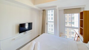 A hotel room with a bed, a television, a window with curtains, and a view of buildings outside. - Chic And Cozy Studio At Tokyo Riverside Pik 2 Apartment (Teluknaga)