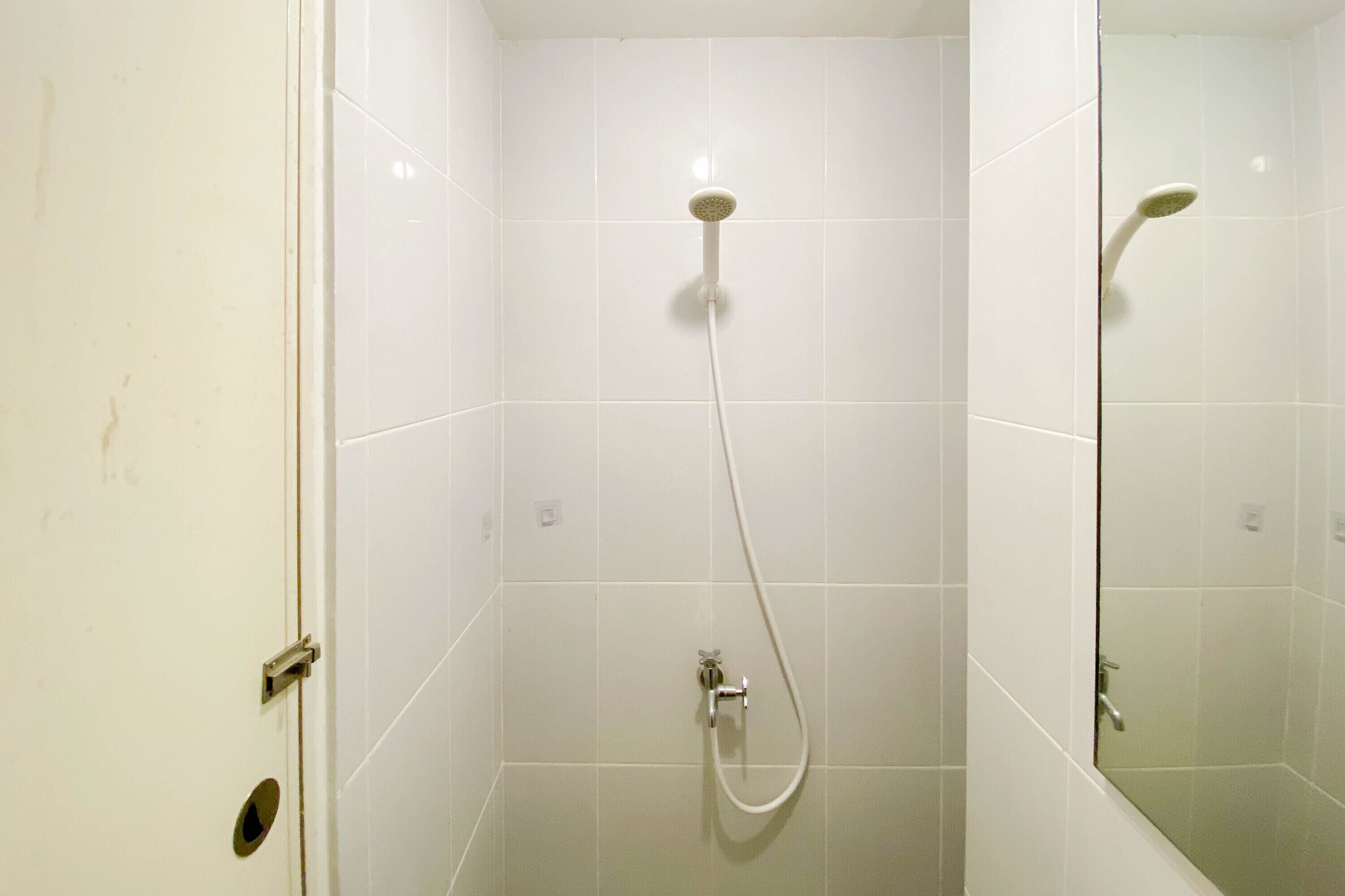 A bathroom with white tiles, a shower with a handheld showerhead, and a mirror on the wall.