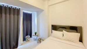 Une chambre d’hôtel avec un lit, des rideaux, une petite table ronde ornée d’une plante et une fenêtre également munie de rideaux.