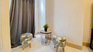 Une petite pièce bien éclairée, avec deux ottomans assortis, une table d’appoint ronde ornée d’une plante et une grande fenêtre avec des rideaux.