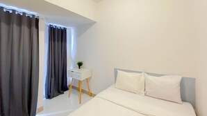 Quarto com cama, mesa de cabeceira com planta e janela com cortinas.