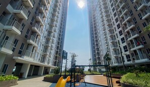 A residential building with multiple floors, balconies, and a playground area with slides and swings. - Homey And New Studio At Tokyo Riverside Pik 2 Apartment (Teluknaga)