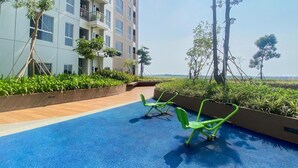 Área de piscina no terraço, com piso azul, equipamentos de ginástica verdes e vegetação ao redor.