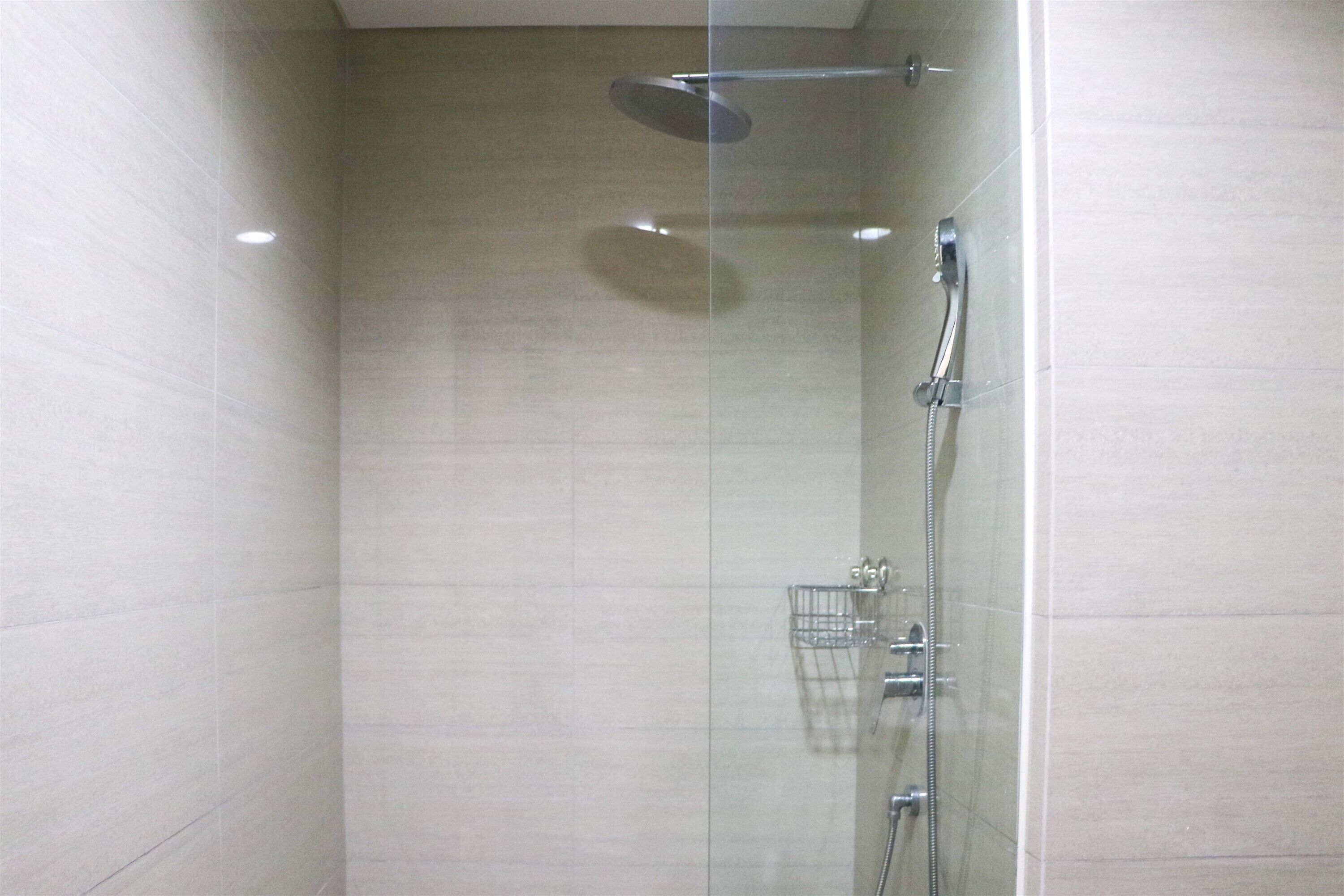 A glass-enclosed shower with a handheld showerhead, a wall-mounted faucet, and a showerhead.