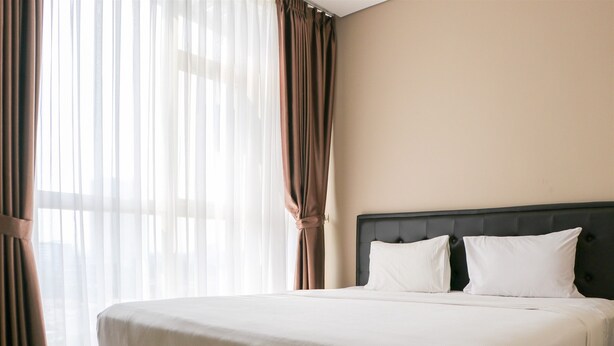 A hotel room with a large bed, a headboard, and sheer curtains. - Spacious And Homey 2Br At Ciputra International Apartment (Jakarta)