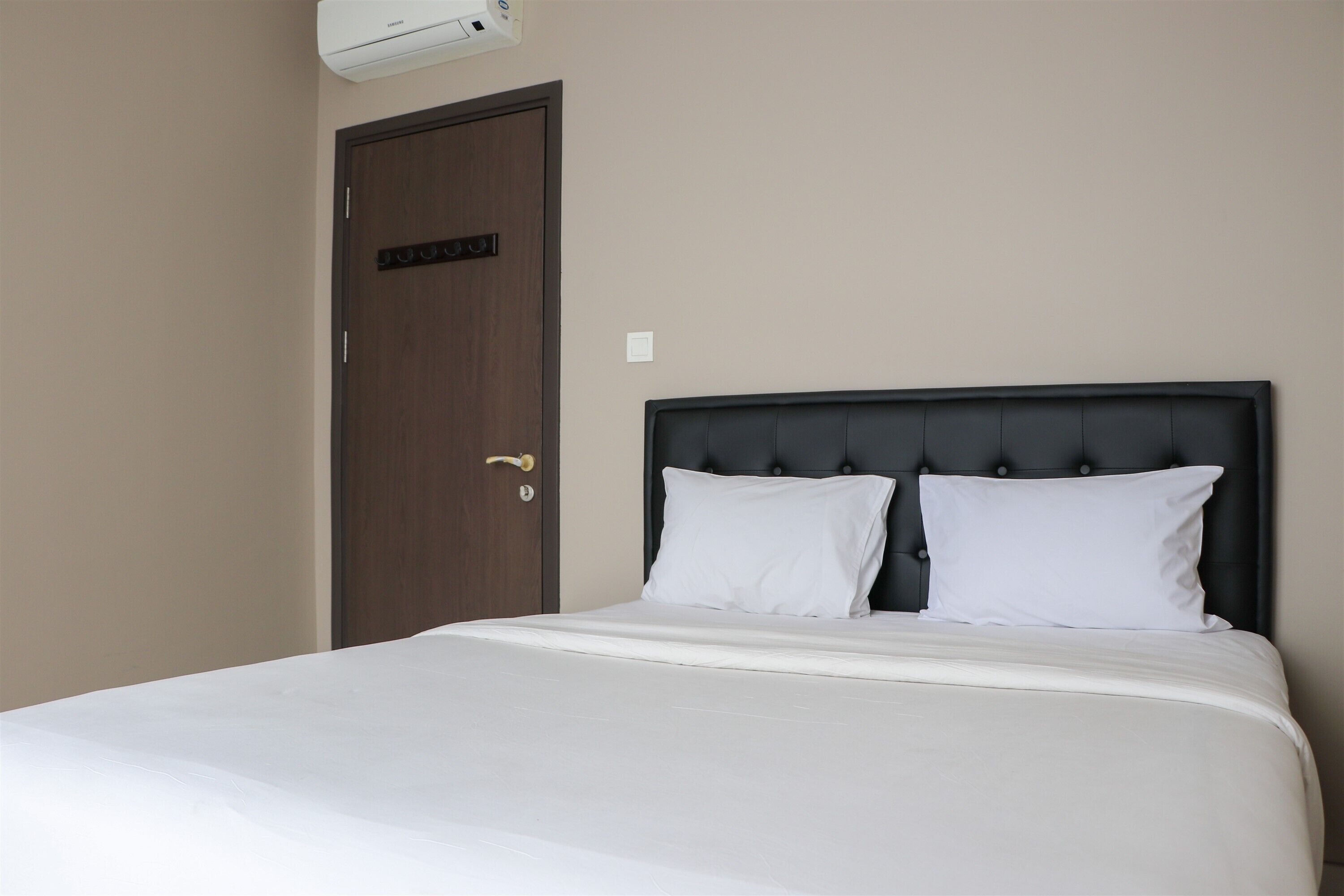 A hotel room with a bed, a door, and an air conditioning unit.