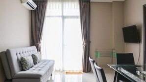 A modern living room with a grey sofa, a glass dining table, and a mounted TV. - Spacious And Homey 2Br At Ciputra International Apartment (Jakarta)
