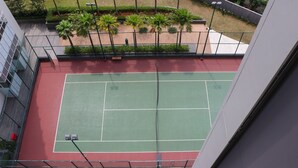 A tennis court with a red and green surface, surrounded by a fence and palm trees. - Spacious And Homey 2Br At Ciputra International Apartment (Jakarta)