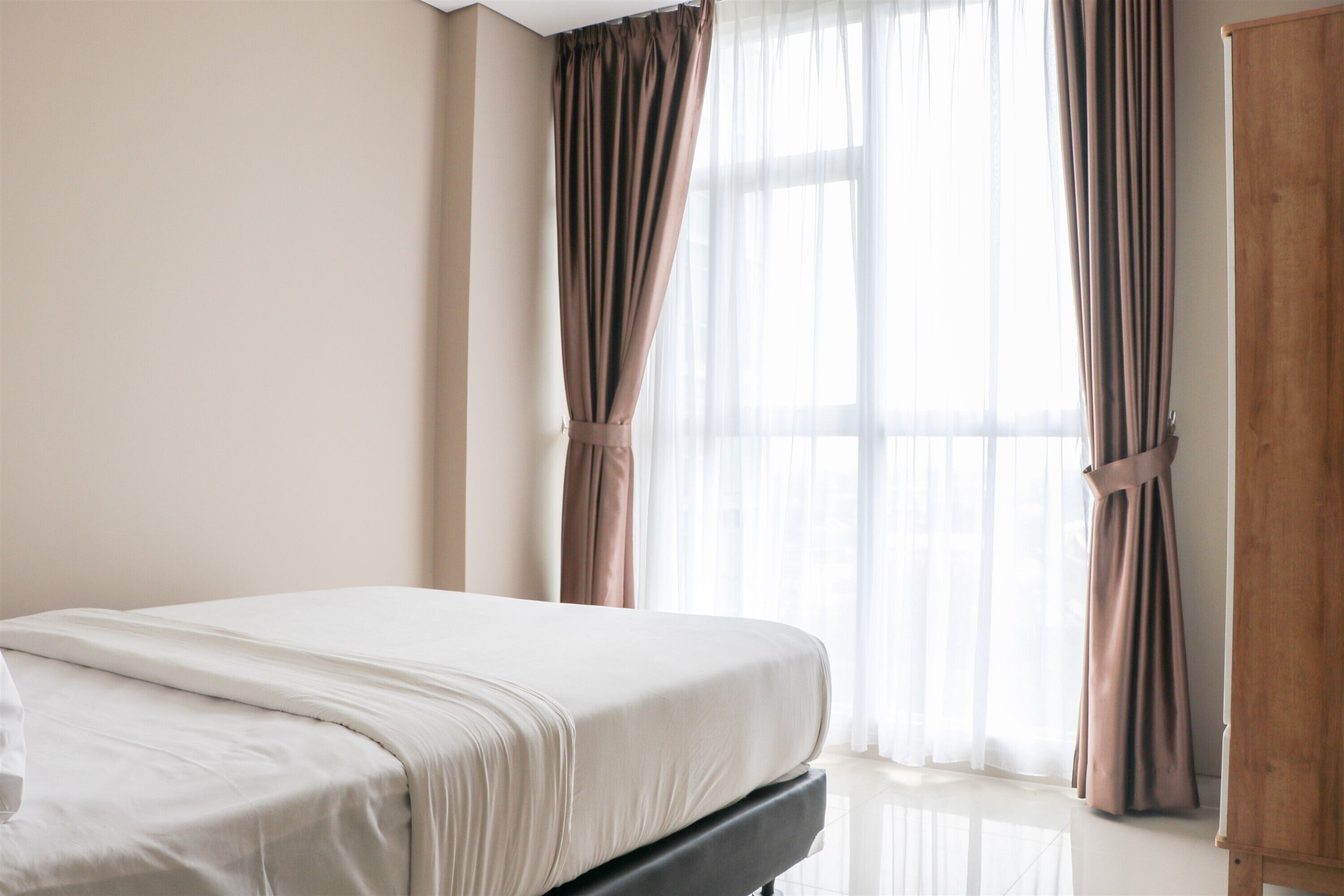 A bedroom with a bed, a wooden wardrobe, and sheer curtains.