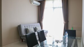 A modern living room with a grey sofa, a glass table with chairs, and an air conditioning unit on the wall. - Spacious And Homey 2Br At Ciputra International Apartment (Jakarta)