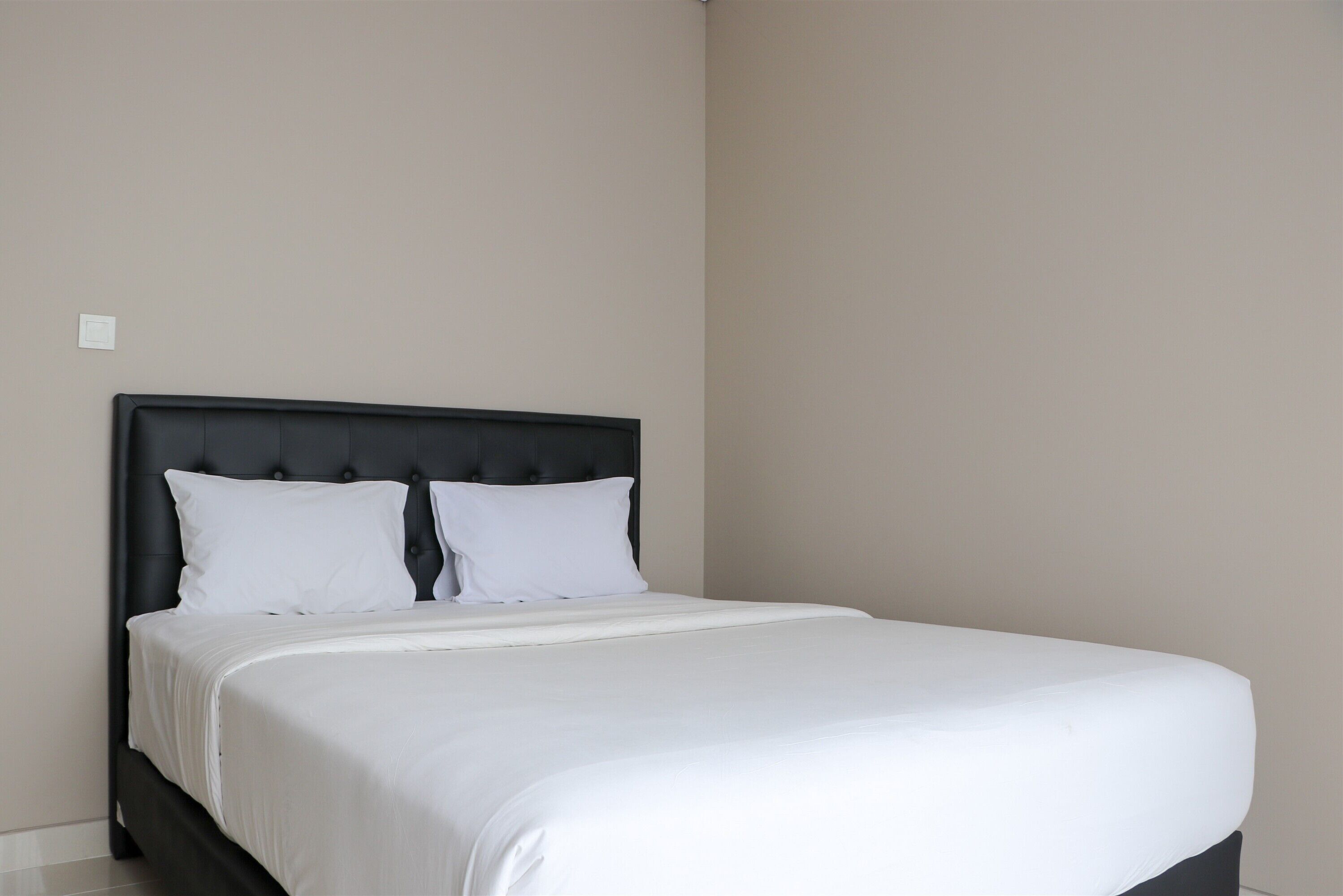 A neatly made bed with a black headboard and white bedding in a room with plain walls.