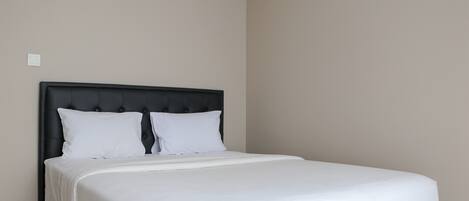 A neatly made bed with a black headboard and white bedding in a room with plain walls.