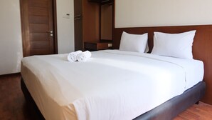 Ein ordentlich bezogenes Bett mit weißen Laken und zwei Kissen, ein Holz-Kopfbrett und eine Holztür zur Linke.