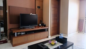 Ein modernes Wohnzimmer mit einem Flachbildfernseher auf einer Holz-Unterhaltungseinheit, einem Couchtisch mit Blumenvase und einer Tür rechts.