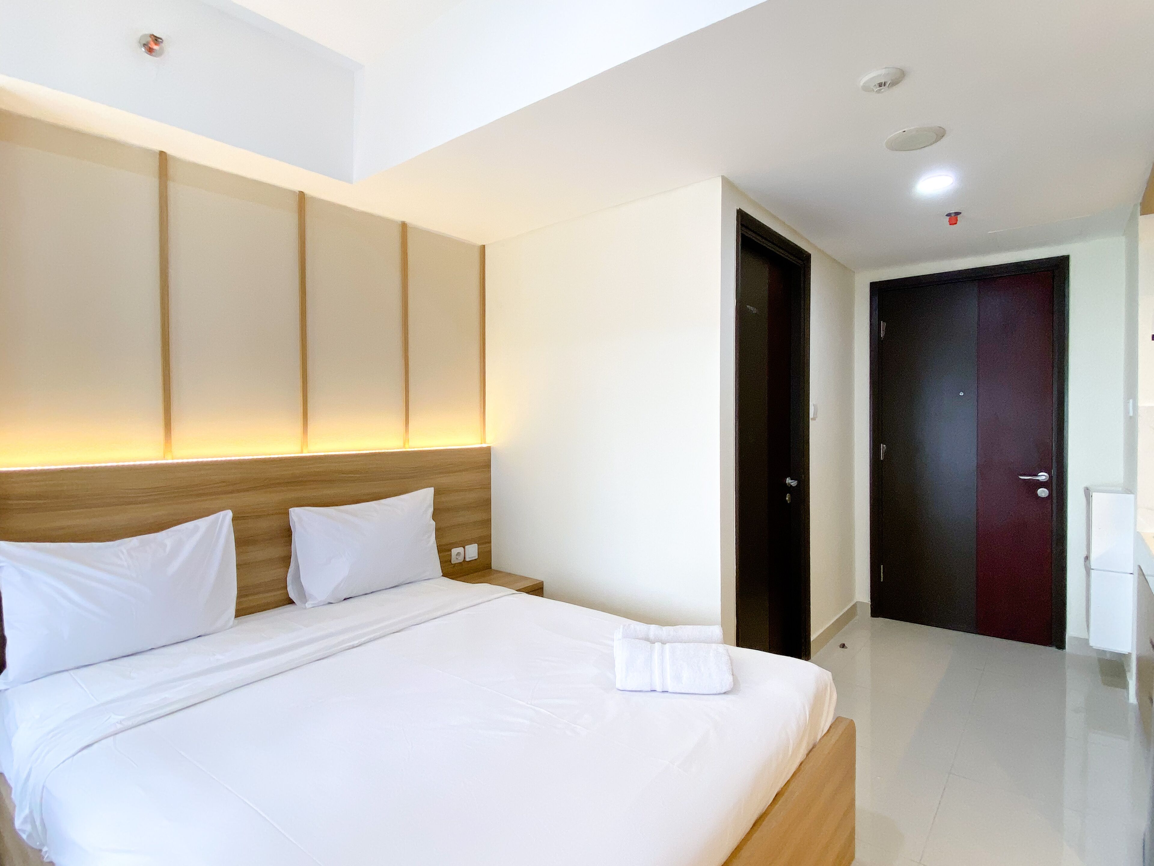 A modern hotel room with a large bed, a wooden headboard, and a dark door.