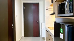 A compact kitchen with a microwave, refrigerator, and a door leading to another room. - Homey And Warm Studio Room Pollux Chadstone Apartment (Cikarang)