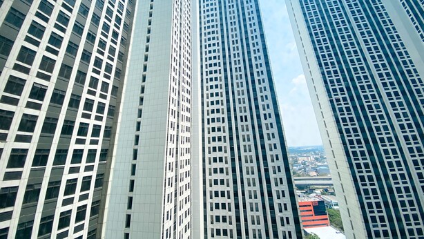 A high-rise building with a grid of windows and a clear sky in the background. - Homey And Warm Studio Room Pollux Chadstone Apartment (Cikarang)