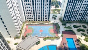 An aerial view of a residential complex with high-rise buildings, a basketball court, a swimming pool, and landscaped areas. - Homey And Warm Studio Room Pollux Chadstone Apartment (Cikarang)