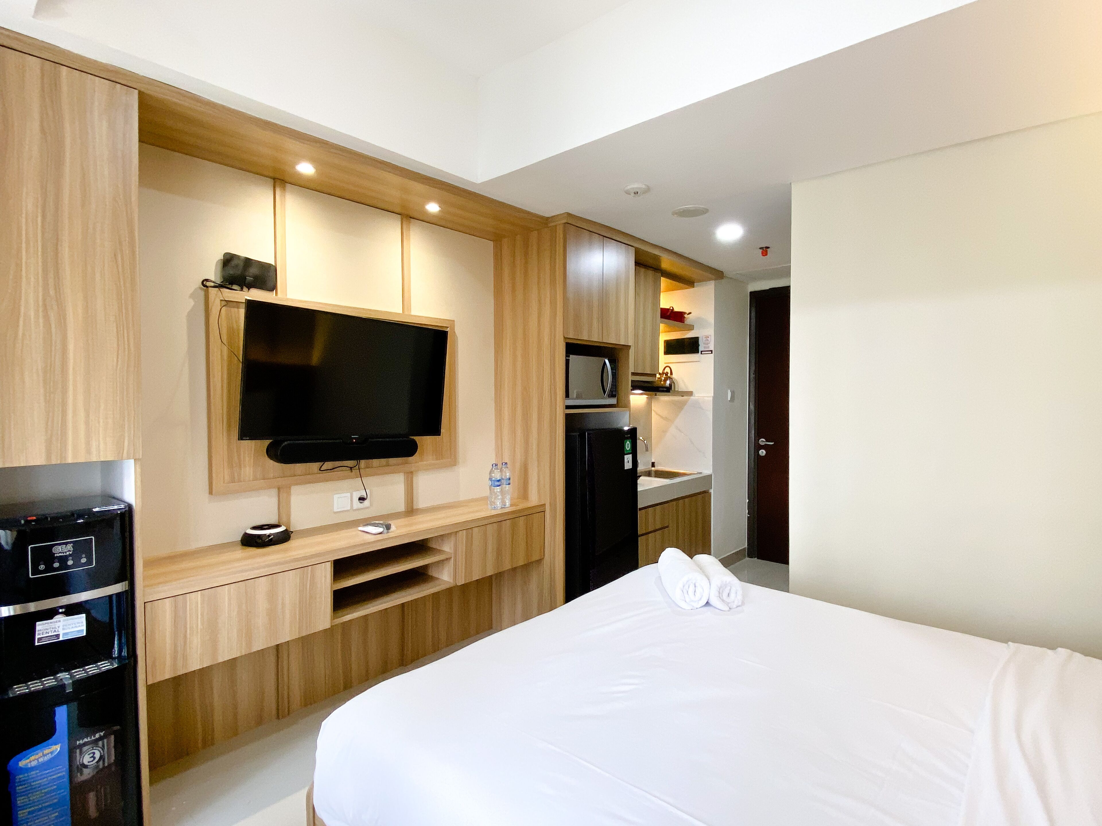 Een hotelkamer met een bed, een aan de muur bevestigde televisie, een minibar en een kleine kitchenette.