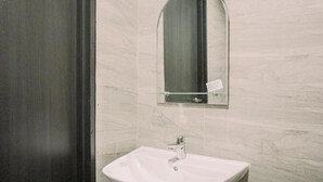 Een badkamer met een wit wastafelmeubel, een spiegel en een marmeren wand.