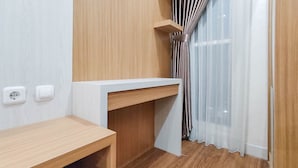 Een kleine, moderne kamer met een houten bureau, een wit schap en een raam met transparante gordijnen.