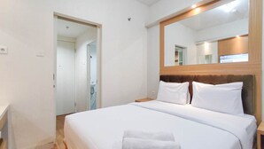Een hotelkamer met een groot bed, een houten hoofdeinde, een spiegel en een deur naar de badkamer.