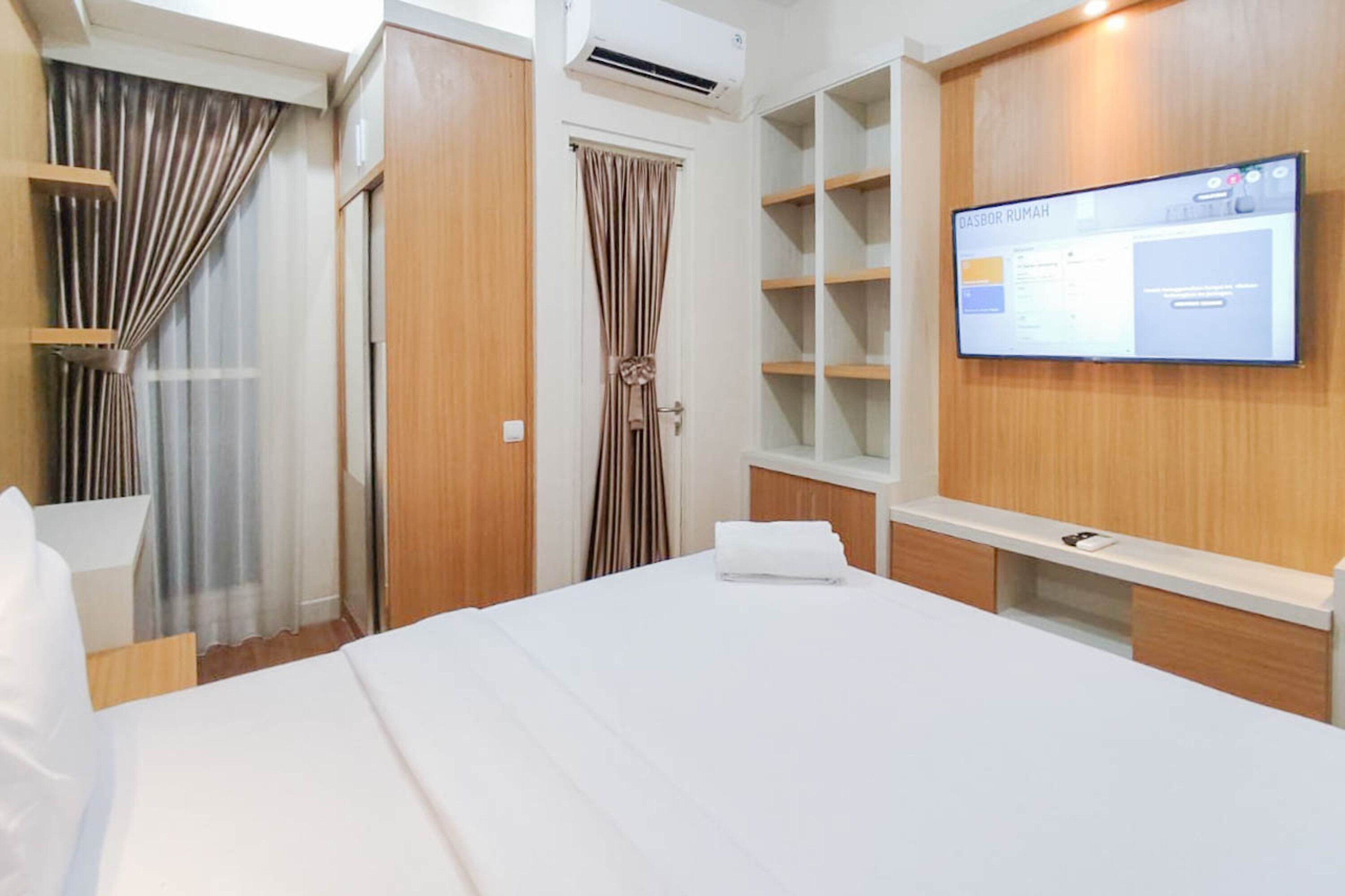 A hotel room with a bed, a TV mounted on the wall, a wardrobe, and a window with curtains.