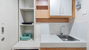 Een compacte keuken met witte aanrechtbladen, een roestvrijstalen spoelbak, houten kastjes en een klein plankje met keukengerei.