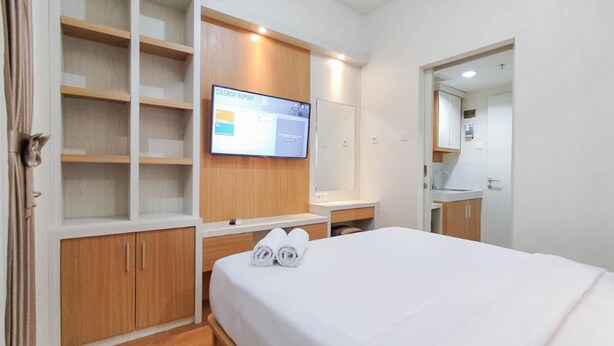 Een hotelkamer met een bed, een aan de muur bevestigde televisie, een houten garderobe en een badkamer zichtbaar door een open deur.
