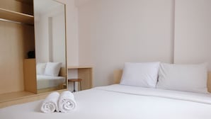 Habitación de hotel con una cama bien hecha, un armario de madera, una pequeña mesa redonda y un espejo grande.
