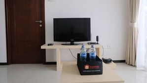Habitación de hotel con un escritorio de madera, un televisor de pantalla plana, un control remoto, un portal botellas para dos botellas y un altavoz pequeño.