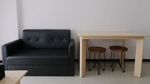 Un sofá de cuero negro, una mesa de madera con dos taburetes y una mesita de madera.
