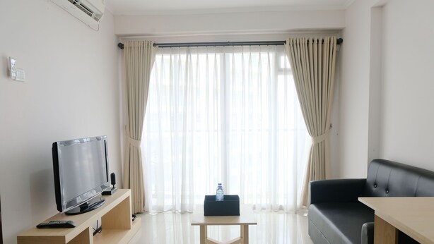 Una sala de estar moderna con un televisor de pantalla plana sobre un mueble de madera, un sofá de cuero negro, una mesa de centro de madera y un ventanal con cortinas translúcidas.
