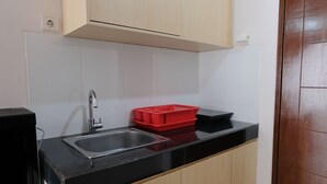 Una cocina con encimera negra, pileta de acero inoxidable, armarios de madera y un escurreplatos rojo.