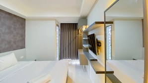 A modern hotel room with a large bed, a bedside table, a mirror, and a built-in shelf with books and a remote control. - Modern And Homey 1Br (No Kitchen) Gold Coast Apartment (Jakarta)