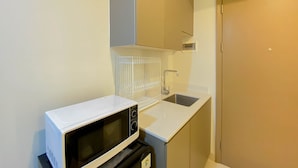 A compact kitchenette with a microwave, sink, and cabinet. - Modern And Homey 1Br (No Kitchen) Gold Coast Apartment (Jakarta)