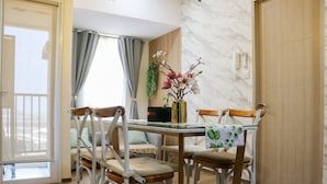 A dining area with a glass table, four chairs, a vase with flowers, a plant, and a wooden door. - Cozy Stay And Minimalist 1Br Tokyo Riverside Pik 2 Apartment (Teluknaga)