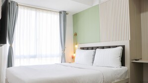 A neatly made bed with white linens, a bedside lamp, and a view of the room's interior. - Cozy Stay And Minimalist 1Br Tokyo Riverside Pik 2 Apartment (Teluknaga)
