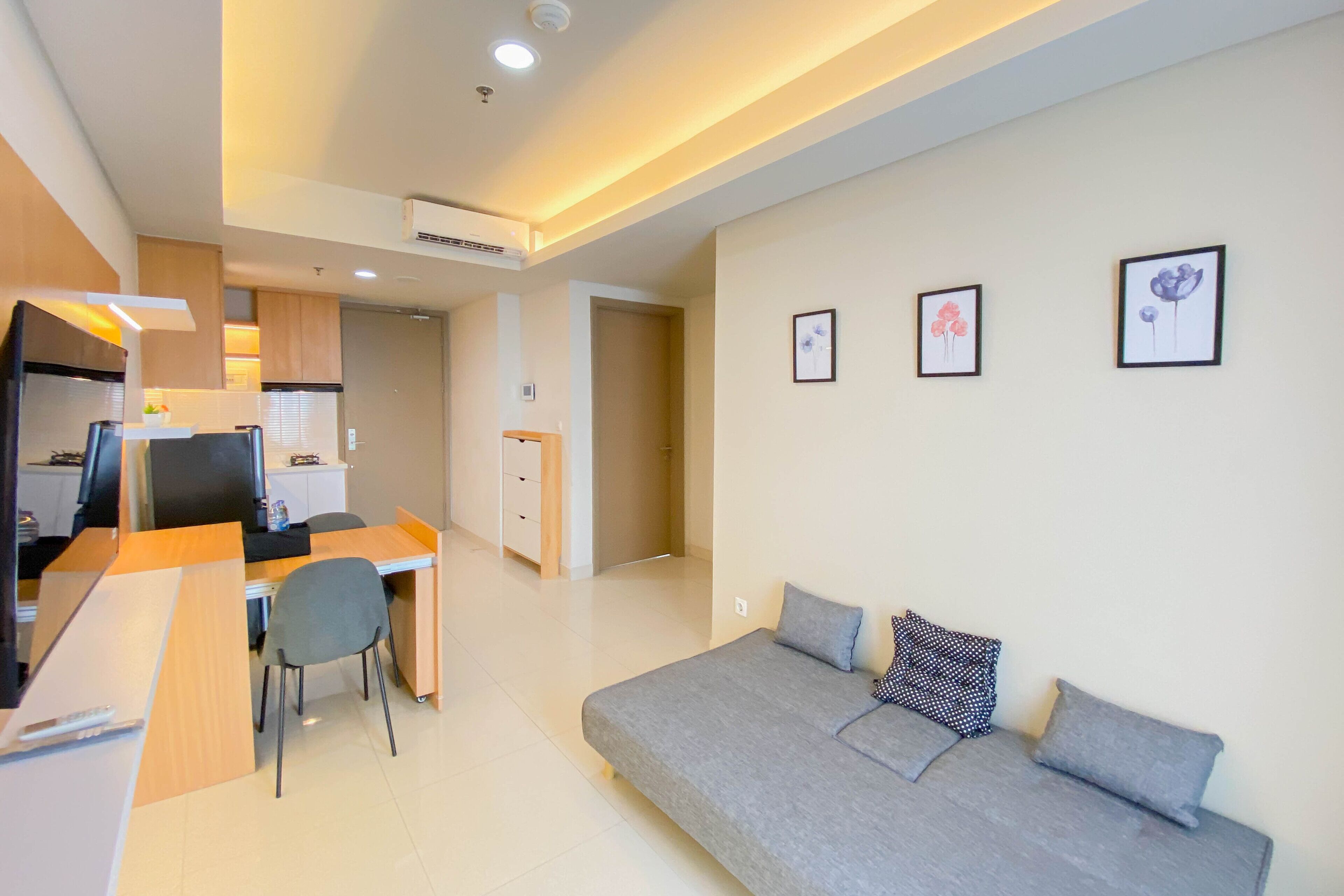 A modern living room with a grey sofa, a wooden desk, and a chair. There are three framed pictures on the wall.
