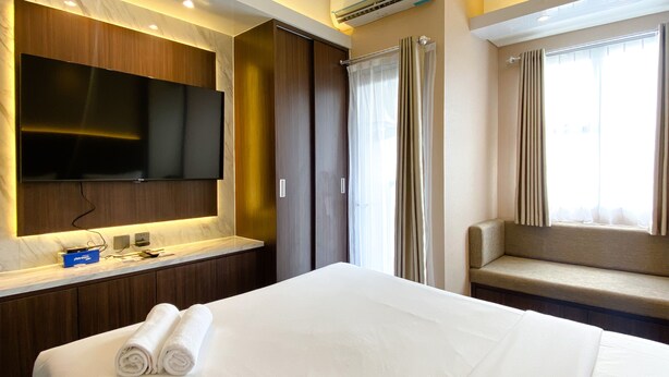 Une chambre d’hôtel dotée d’un grand lit, d’un téléviseur à écran plat fixé au mur, d’un bureau intégré avec un miroir et d’une fenêtre avec des rideaux.