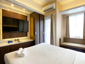 Hotellihuone, jossa on suuri sänky, seinälle asennettu taulutelevisio, sisäänrakennettu työpöytä peilillä sekä ikkuna, jossa on verhot.