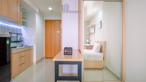 A compact hotel room with a kitchenette, a small table, a bed with a nightstand, and a sliding door closet. - Simply Look Studio High Fl At Evenciio Margonda Apartment (Depok)